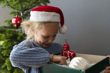 Mädchen mit Weihnachtsmannmütze, das eine Schachtel mit Weihnachtsdekoration zu Hause hält - SVKF01623