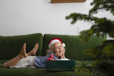 Lächelndes Mädchen auf dem Sofa liegend mit einer Schachtel Weihnachtsschmuck - SVKF01624