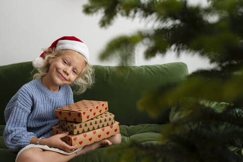 Lächelndes Mädchen mit Weihnachtsgeschenken auf dem Sofa zu Hause - SVKF01632