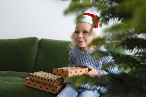 Glückliches Mädchen mit Weihnachtsgeschenken auf dem Sofa zu Hause - SVKF01633