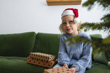 Nachdenkliches Mädchen sitzt mit Weihnachtsgeschenken zu Hause - SVKF01634