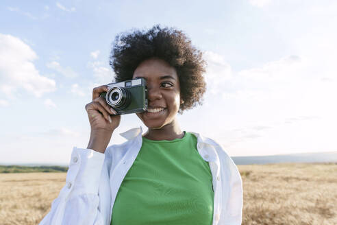 Lächelnde Frau, die durch eine Kamera im Feld fotografiert - AAZF01085