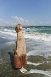 Frau mit geschlossenen Augen steht am Strand in der Nähe des Meeres - SIF00944