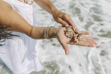 Frau hält Armband aus Muscheln in der Hand am Meer - SIF00951