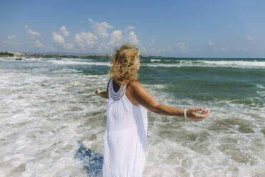 Frau mit ausgestreckten Armen steht inmitten von Wellen im Meer am Strand - SIF00955