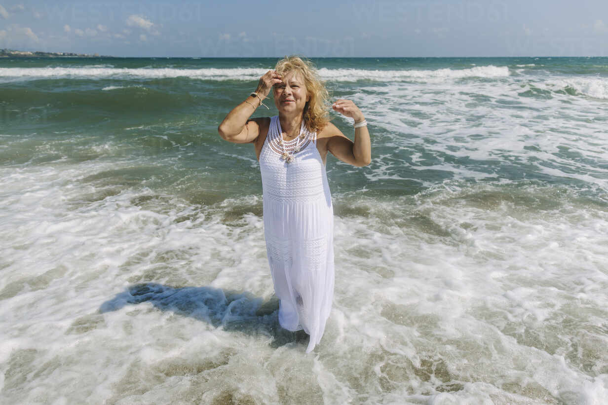 Senior woman wearing dress standing on shore at beach stock photo