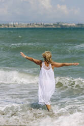 Carefree woman with arms outstretched walking in sea at beach - SIF00961