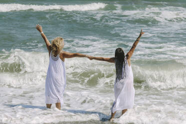 Carefree friends with hands raised standing in sea at beach - SIF00967
