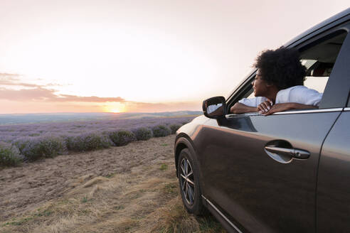 Young woman looking though car window at sunset - AAZF01135