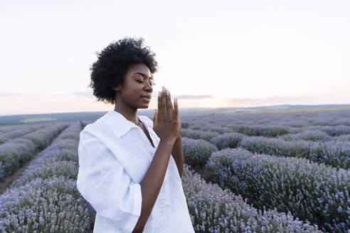 Junge Frau mit Gebetshaltung im Lavendelfeld stehend - AAZF01140