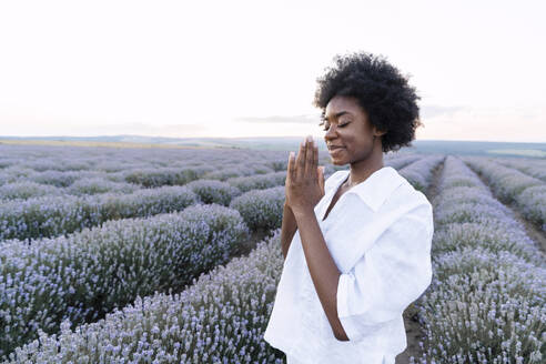 Smiling woman with prayer pose standing in lavender field - AAZF01141