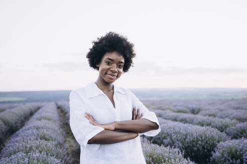Smiling woman with arms crossed standing in lavender field - AAZF01145