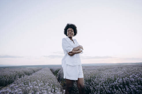 Happy woman with arms crossed standing in lavender field - AAZF01146