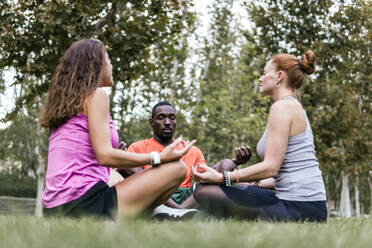 Multi-ethnicl friends practicing lotus position in park - PBTF00267