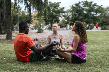 Multi-ethnic friends sitting in lotus position meditating at park - PBTF00268