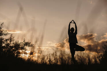 Silhouette woman practicing tree pose yoga at sunset - LLUF01081