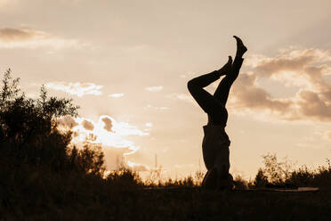 Silhouette einer Frau, die bei Sonnenuntergang Kopfstand-Yoga übt - LLUF01084
