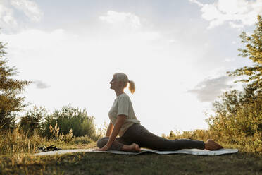 Woman practicing yoga on mat near plants - LLUF01087