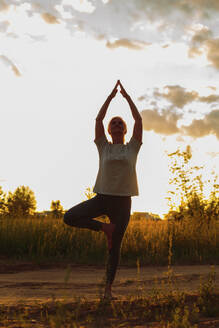 Ältere Frau übt Baumpose Yoga bei Sonnenuntergang - LLUF01092