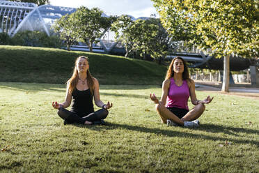 Women practicing Lotus position sitting on grass at park - PBTF00276