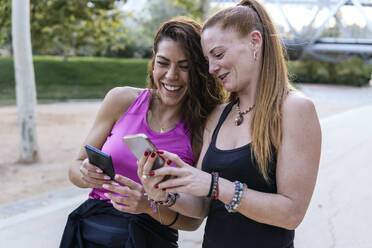 Lächelnde Freunde mit gemeinsamen Smartphones im Park - PBTF00284