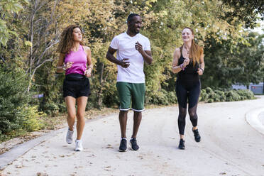 Glückliche multirassische Freunde, die zusammen im Park laufen - PBTF00289