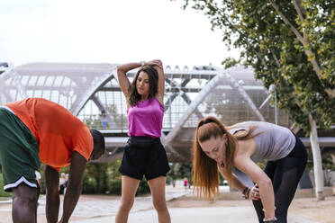 Friends doing warm up stretching at park - PBTF00301