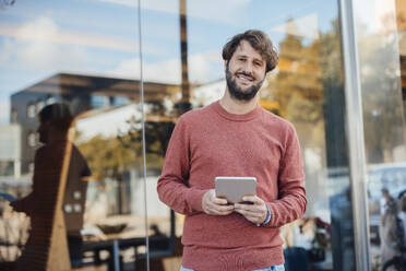 Lächelnder Geschäftsmann mit Tablet-PC vor einem Bürogebäude - JOSEF21053