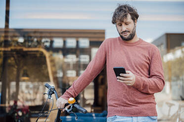 Mann, der ein Smartphone benutzt, steht mit dem Fahrrad vor einer Glaswand - JOSEF21056