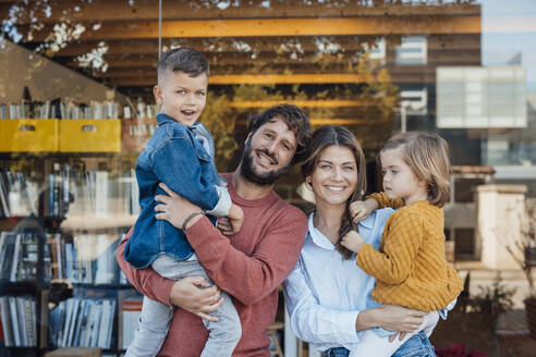 Happy parents with son and daughter in front of glass wall - JOSEF21060