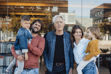 Grandfather standing with family in front of glass wall - JOSEF21063