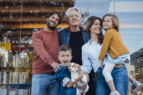 Happy family with dog in front of glass wall - JOSEF21065