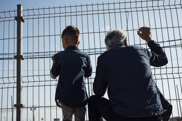 Grandson and grandfather looking through fence - JOSEF21077