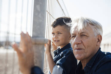 Boy and senior man looking through fence - JOSEF21080
