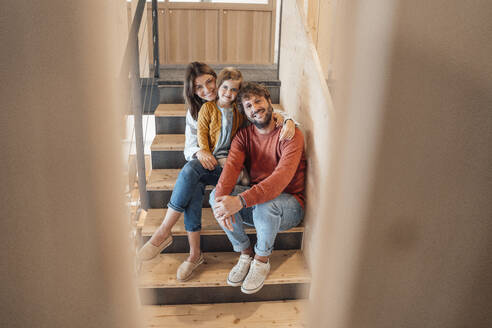 Lächelnder Mann sitzt mit Frau und Tochter auf einer Treppe zu Hause - JOSEF21089