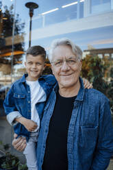 Smiling senior man with grandson standing near wall - JOSEF21098