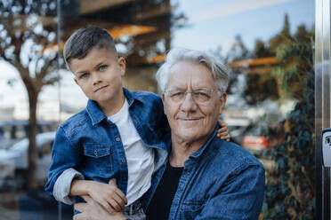 Smiling retired senior man with grandson in front of wall - JOSEF21102