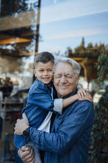 Lächelnder älterer Mann, der einen Jungen vor einer Mauer umarmt - JOSEF21103