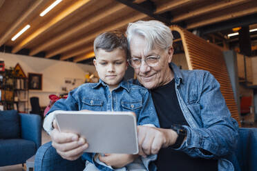 Smiling senior man sharing tablet PC with boy at home - JOSEF21107