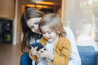 Happy daughter using smart phone with mother at home - JOSEF21130