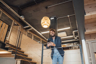 Lächelnder Geschäftsmann lehnt am Geländer im Büro - JOSEF21135