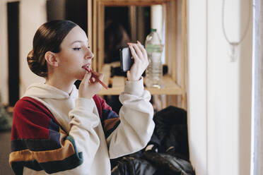 Young woman applying lipstick looking in smart phone - MRRF02689