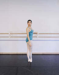 Mädchen im Ballettkostüm steht in der Nähe des Geländers in einer Tanzschule - MRRF02720