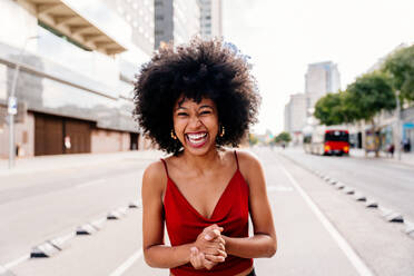 Eine junge afrikanische Studentin mit Afro-Lockenfrisur genießt einen Spaziergang durch die Stadt und strahlt dabei vor Freude - DMDF05964