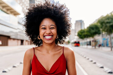 Eine junge afrikanische Frau mit Afro-Lockenfrisur genießt einen Spaziergang durch die Stadt - eine fröhliche schwarze Studentin in Bewegung - DMDF05965