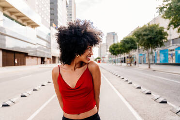 Eine junge, glückliche schwarze Studentin mit Afro-Lockenfrisur genießt einen Spaziergang in der Stadt - DMDF05966