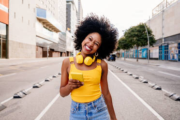 Eine junge afrikanische Frau mit Afro-Lockenfrisur genießt einen Spaziergang durch die Stadt und strahlt als glückliche schwarze Studentin in Bewegung - DMDF05969