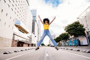 Junge, glückliche afrikanische Frau mit Afro-Lockenfrisur genießt einen Spaziergang durch die Stadt - eine fröhliche schwarze Studentin in Bewegung - DMDF05976