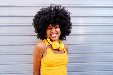 Schöne junge glückliche afrikanische Frau mit Afro-Lockenfrisur schlendert in der Stadt - Fröhliche schwarze Studentin Porträt auf bunten Wand Hintergrund - DMDF05979