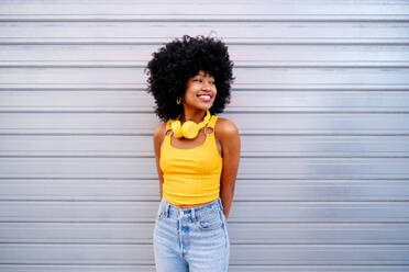 Beautiful young happy african woman with afro curly hairstyle strolling in the city - Cheerful black student portrait on colorful wall background - DMDF05980